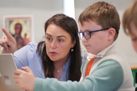 Múinteoir agus páiste ag faire ar scáileán ríomhaire