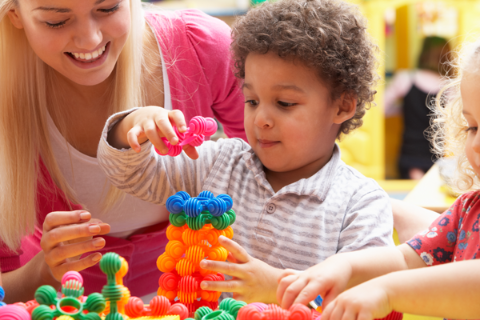 Early Childhood practitioner encouraging a child to build a tower from colourful, interconnecting blocks
